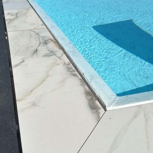 Immagine di bordo piscina con pavimento in gres per piscine a sfioro effetto marmo Calacatta - dettaglio angolo
